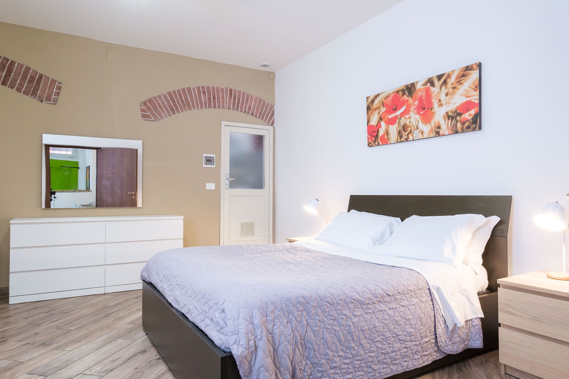 A bedroom with a bed, bedside tables, a dresser, a mirror, and a painting on the wall.