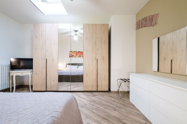 A bedroom with a bed, a desk, a wardrobe, and a ceiling fan.