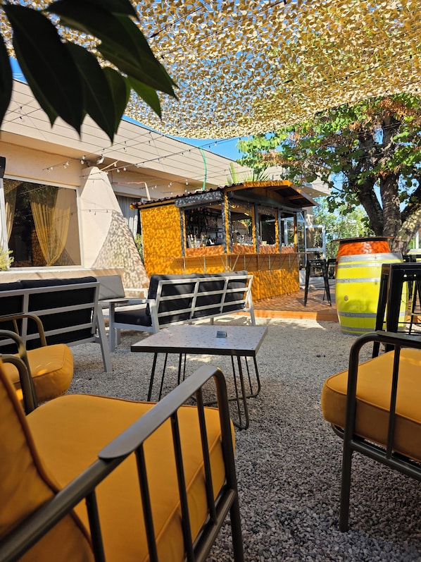 An outdoor seating area with tables and chairs, a bar area, and a decorative canopy. - Logis Hôtel Restaurant Le Pardaillan (Gondrin)