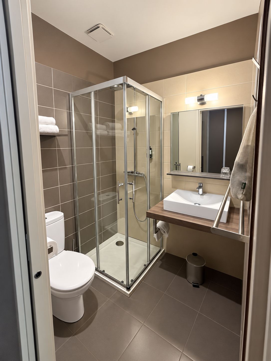 Een moderne badkamer met een douchecabine van glas, een wit toilet en een wastafel met spiegel erboven.