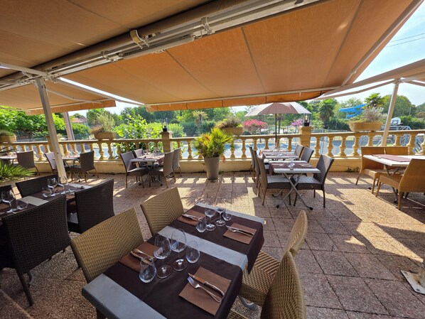 An outdoor patio with tables and chairs, a view of a body of water, and potted plants. - Logis Hôtel Restaurant Le Pardaillan (Gondrin)