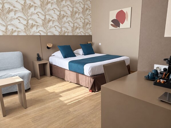 A hotel room with a bed, a desk, a chair, a bedside table, and a wall-mounted coffee machine. - Logis Hôtel Restaurant Le Pardaillan (Gondrin)