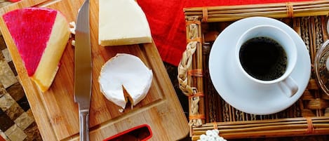 A wooden cutting board with cheese and a knife, a cup of coffee, and a woven mat.