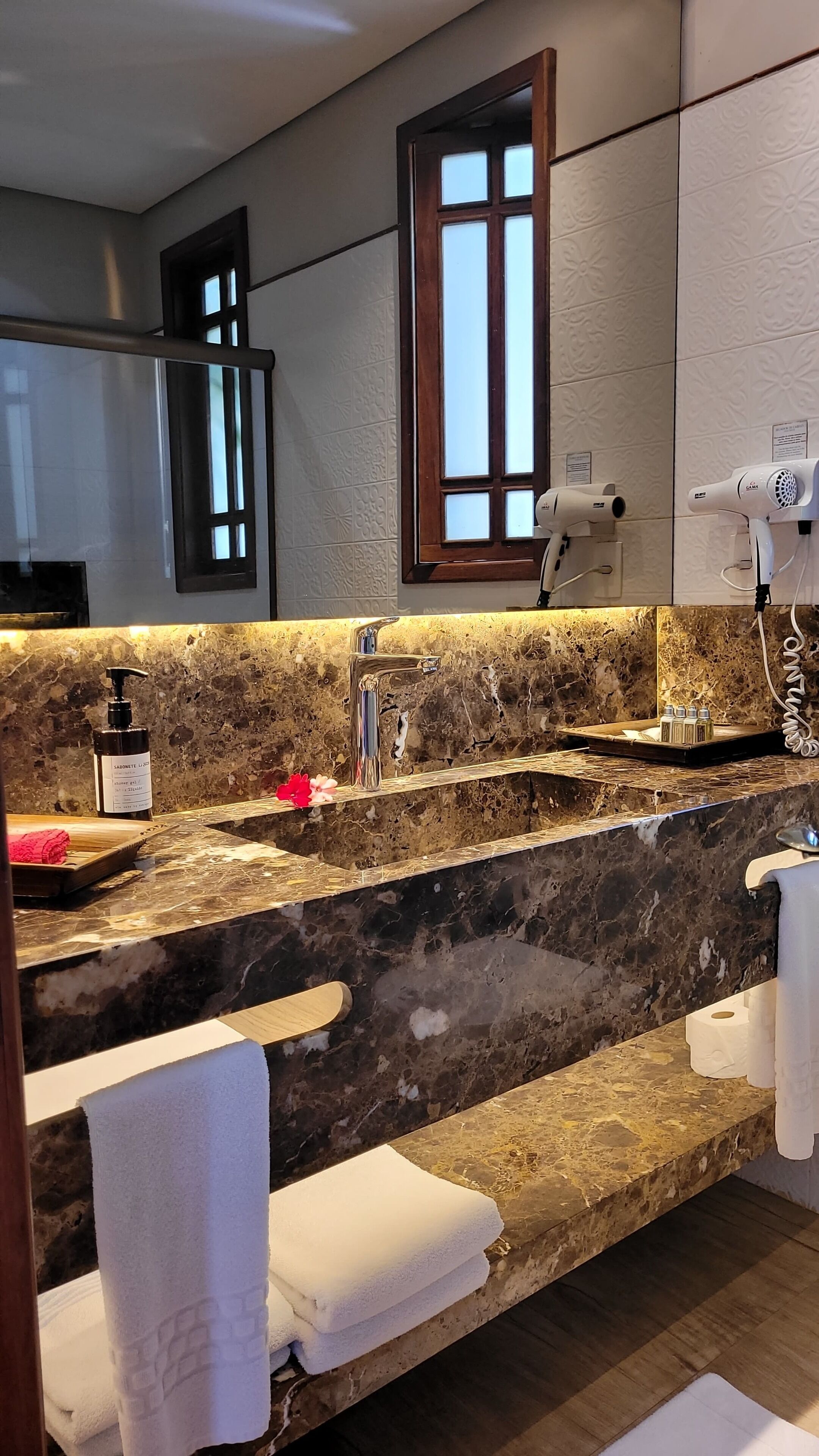 A bathroom with a marble countertop, a sink, a mirror, a window, and a hairdryer.
