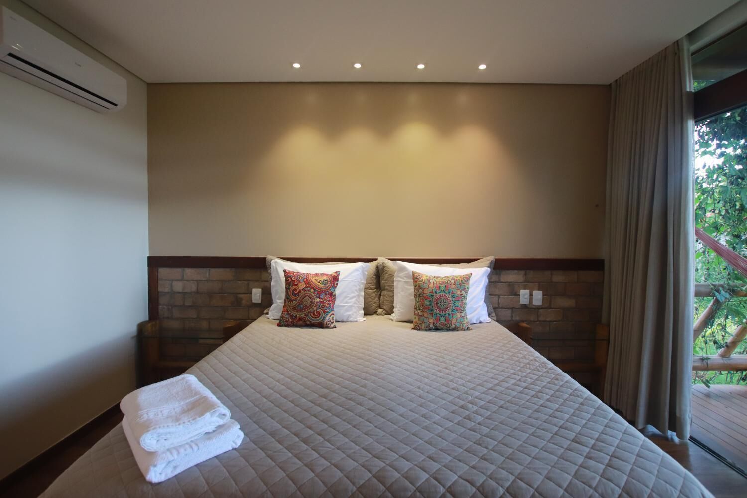 A hotel room with a large bed, two decorative pillows, a neatly folded white towel, and a brick-patterned headboard.