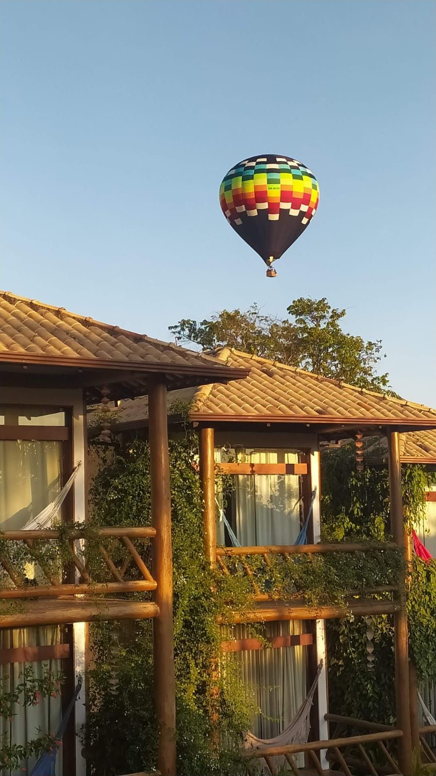 A hot air balloon with a colorful pattern flying above a wooden structure with a tiled roof.