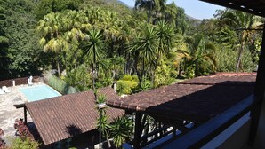 A view from a covered balcony overlooking a swimming pool and lush tropical vegetation. - Pousada Água Cristalina (Cachoeiras de Macacu)