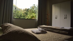 A bedroom with a bed, a wardrobe, and a window with a view of greenery. - Pousada Água Cristalina (Cachoeiras de Macacu)