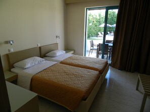 A hotel room with two beds, a window with curtains, and a view of the outdoor area.