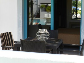 A table with a decorative glass centerpiece, surrounded by wicker chairs, with a view of a pool and outdoor seating in the background. - Triantafillas Appartments (Rhodes)