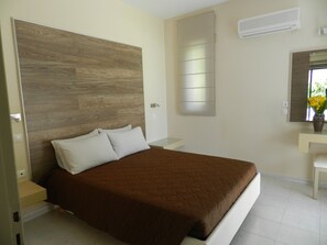 A bedroom with a large bed, a bedside table, a mirror, and an air conditioning unit on the wall. - Triantafillas Appartments (Rhodes)