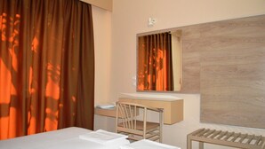 Une chambre d’hôtel avec un lit, un bureau, une chaise, un miroir et une fenêtre avec des rideaux.