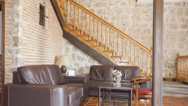Una sala de estar con pared de piedra, escalera de madera, sofás de cuero y una mesa de centro de vidrio.