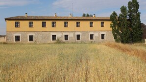 Un edificio largo y amarillo con numerosas ventanas y base de piedra, rodeado por un campo.