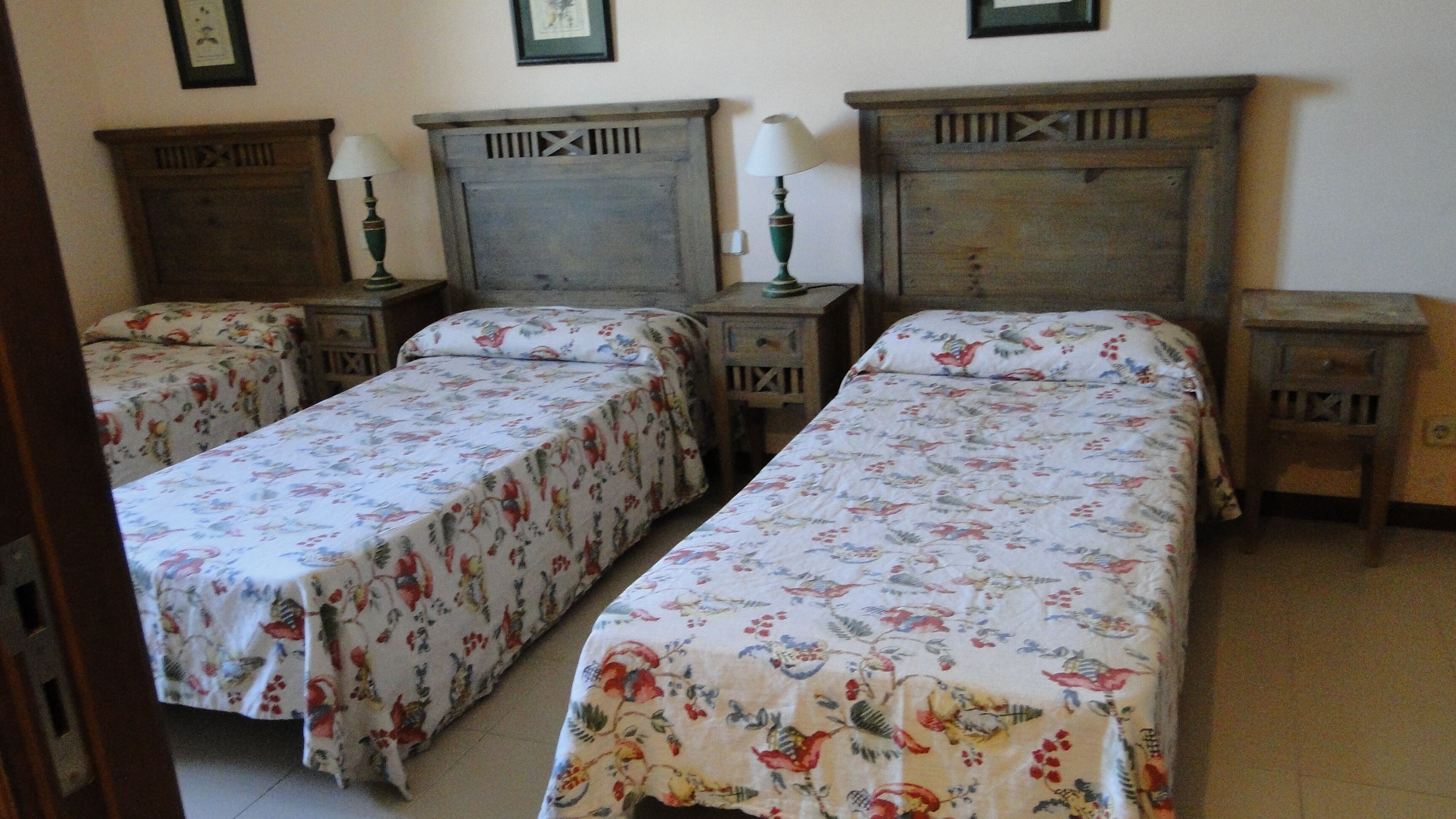 Une chambre dotée de deux lits simples, chacun agrémenté de draps à motifs floraux, de têtes de lit en bois et de tables de chevet avec des lampes.