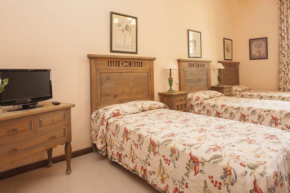 Habitación de hotel con dos camas, un televisor sobre una cómoda de madera y ropa de cama con estampado floral.