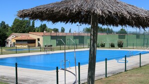 Una piscina con una estructura de techo de paja, rodeada por una valla y un edificio pequeño al fondo.