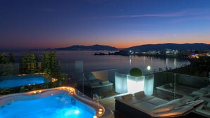 Ein luxuriöses Ambiente im Freien mit Whirlpool, Liegestühlen und Blick auf das Meer im Abendrot.