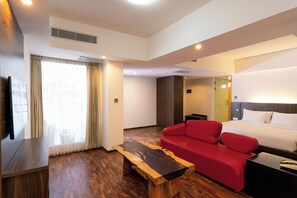 A hotel room with a wooden floor, a red sofa, a bed with white linens, a wooden coffee table, and a TV on a stand. - The Bene Kuta Bali (Kuta)
