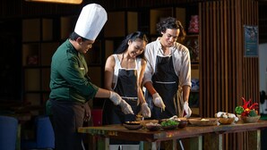 A restaurant interior with a wooden sign reading "Plumeria," a chef in a white hat, and two waitresses in aprons preparing food. - The Bene Kuta Bali (Kuta)