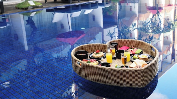 A poolside breakfast setup with a wicker basket containing food and drinks, reflecting the pool's edge. - The Bene Kuta Bali (Kuta)