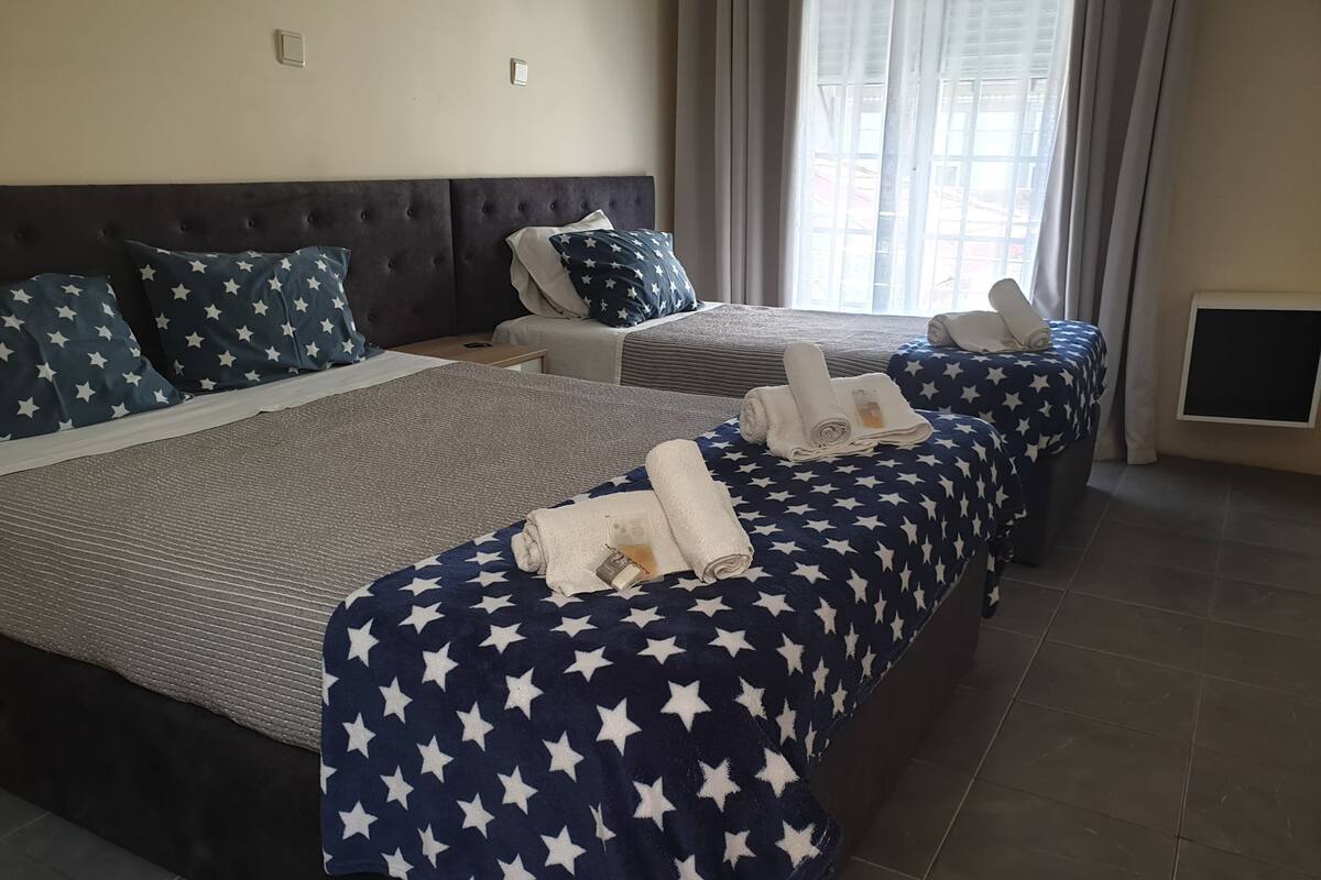 A hotel room with two beds, each with a star-patterned bedspread, a dark headboard, and a window with curtains.