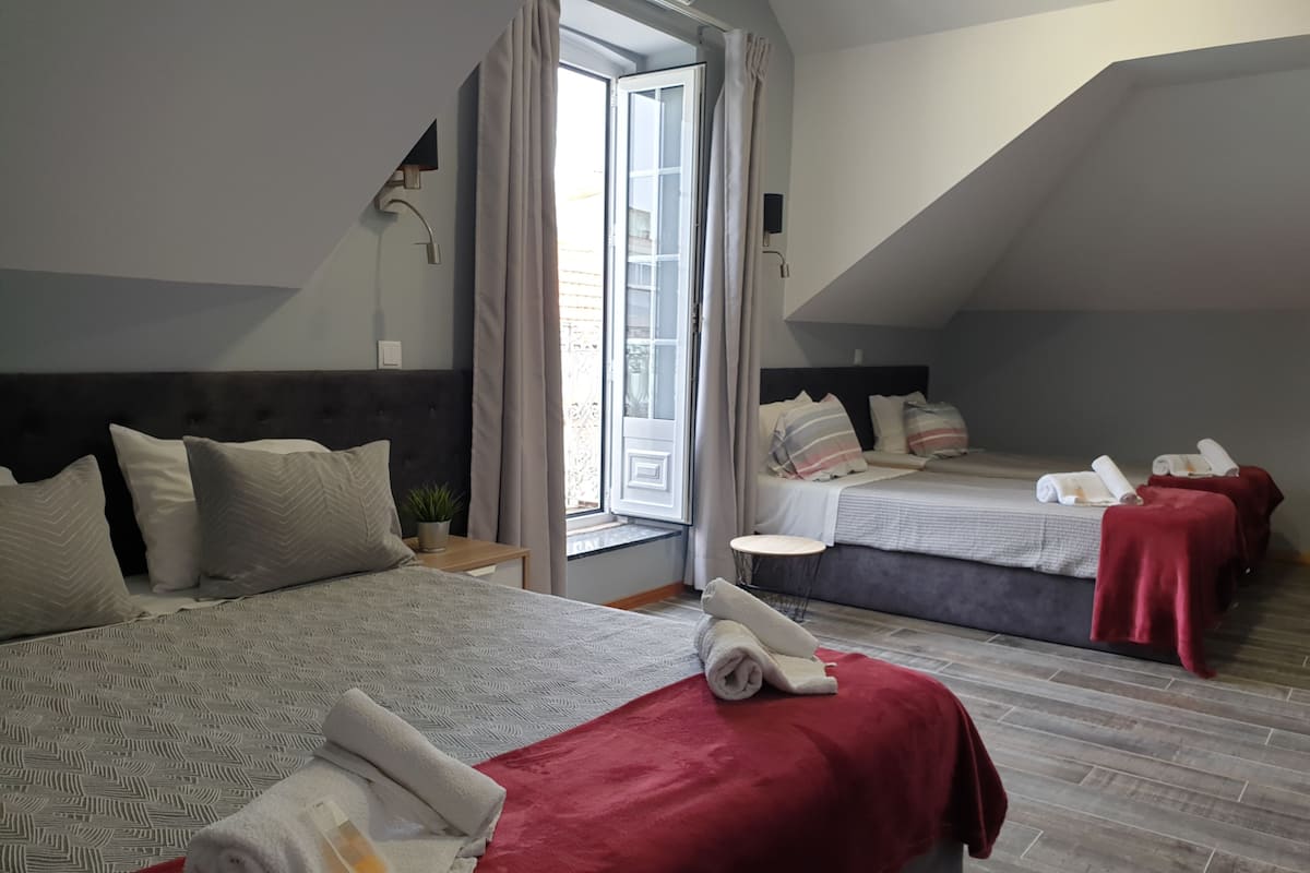 A hotel room with two beds, each with a red blanket and rolled towels. There is a small round table and a potted plant on the left side.