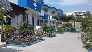 Un hôtel aux murs extérieurs bleus et blancs, doté d’un chemin en béton et agrémenté de diverses plantes à fleurs.
