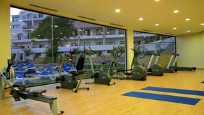 A gym with exercise equipment, large windows, and a view of a building and trees. - Cerro Mar Garden (Albufeira)
