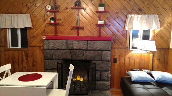 Una habitación acogedora con chimenea de piedra, paredes de madera, una mesa de comedor y un sofá.