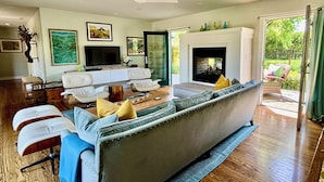 Ein modernes Wohnzimmer mit einem großen grauen Sofa, weißen Sesseln, einem Flachbildfernseher und einem Kamin.