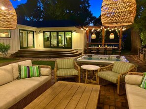 Een terras buiten met rieten meubilair, een jacuzzi en een overdekte zithoek met lichtjes.