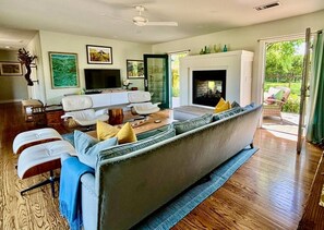 Una sala de estar con sofá, televisor, chimenea y vistas al exterior.