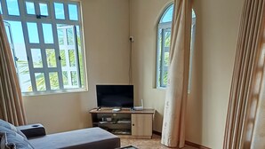 A modern living room with a sectional sofa, a flat-screen TV, a desk, and a large window with curtains.