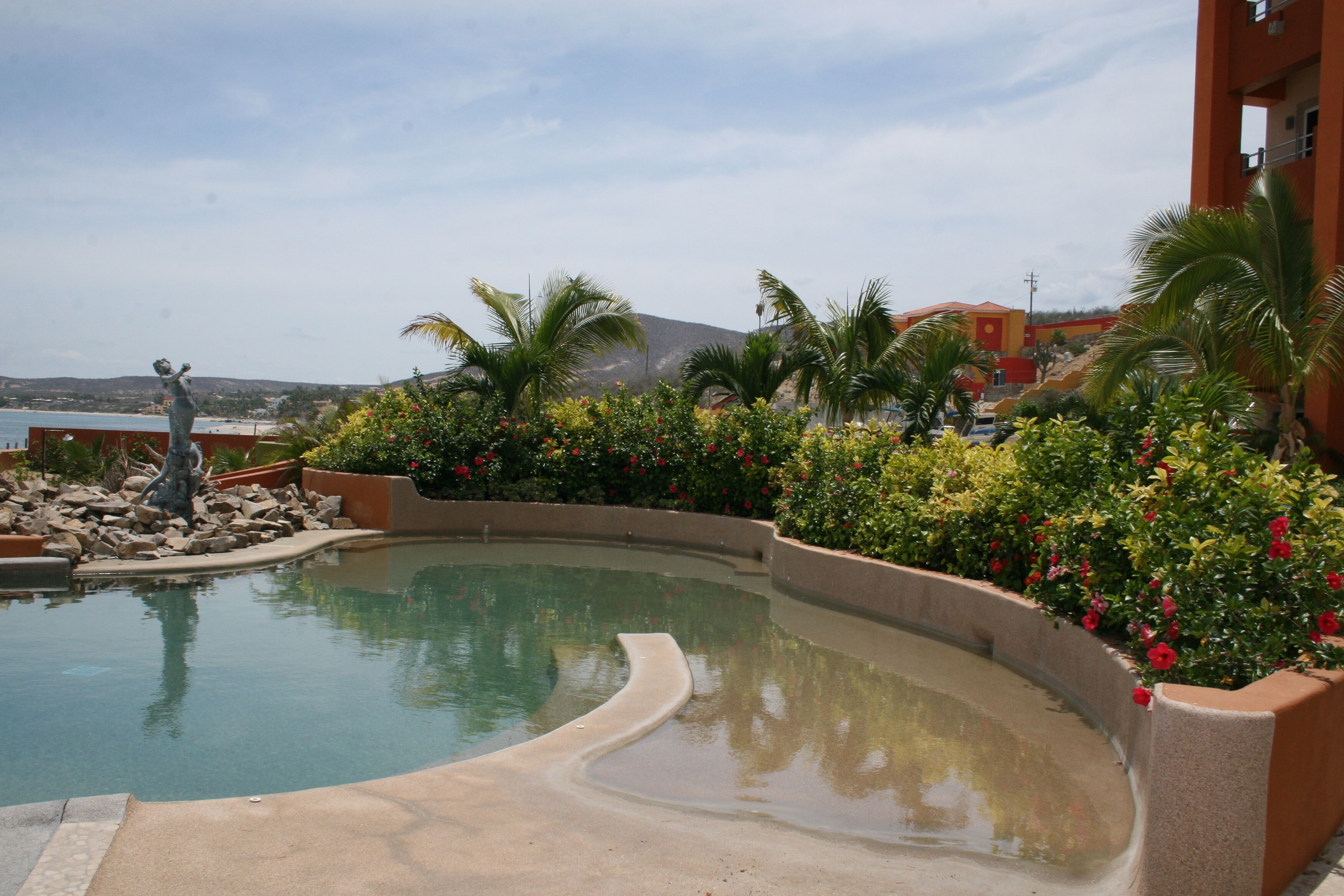 A swimming pool with a curved edge, surrounded by lush greenery and a statue.