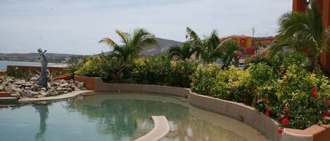 A swimming pool with a curved edge, surrounded by lush greenery and a statue.