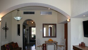Amplia sala de estar con un sofá, una mesa de comedor con sillas, un espejo grande y un televisor sobre un mueble.