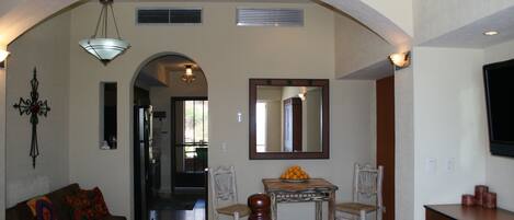 Uma sala de estar ampla com um sofá, uma mesa de jantar com cadeiras, um espelho grande e uma televisão sobre um móvel.