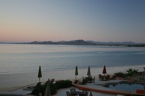 Ein Poolbereich eines Resorts mit Liegestühlen und Sonnenschirmen, mit Blick auf ein ruhiges Meer und entfernte Berge.