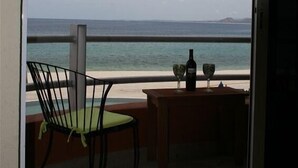 Un balcón con una silla y una mesa, con vista a un cuerpo de agua y terreno lejano.