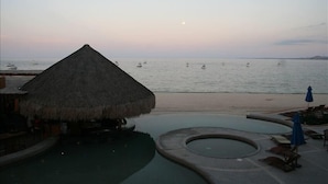 Un resort frente al mar con una cabaña de techo de paja, piscina y sillas de descanso.