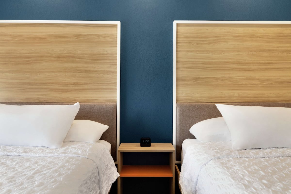 Ein Hotelzimmer mit zwei Betten und einem Nachttisch dazwischen, sowie einer digitalen Uhr.