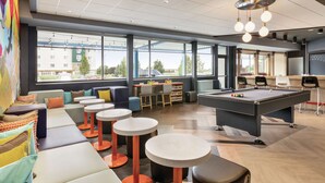 A modern lounge area with a pool table, seating, and large windows offering a view of the outside.