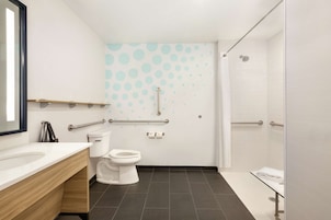 A modern bathroom with a white sink, toilet, and shower area. It includes grab bars and a handrail for accessibility.