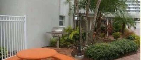 A patio area with a grill, a table, and various plants.