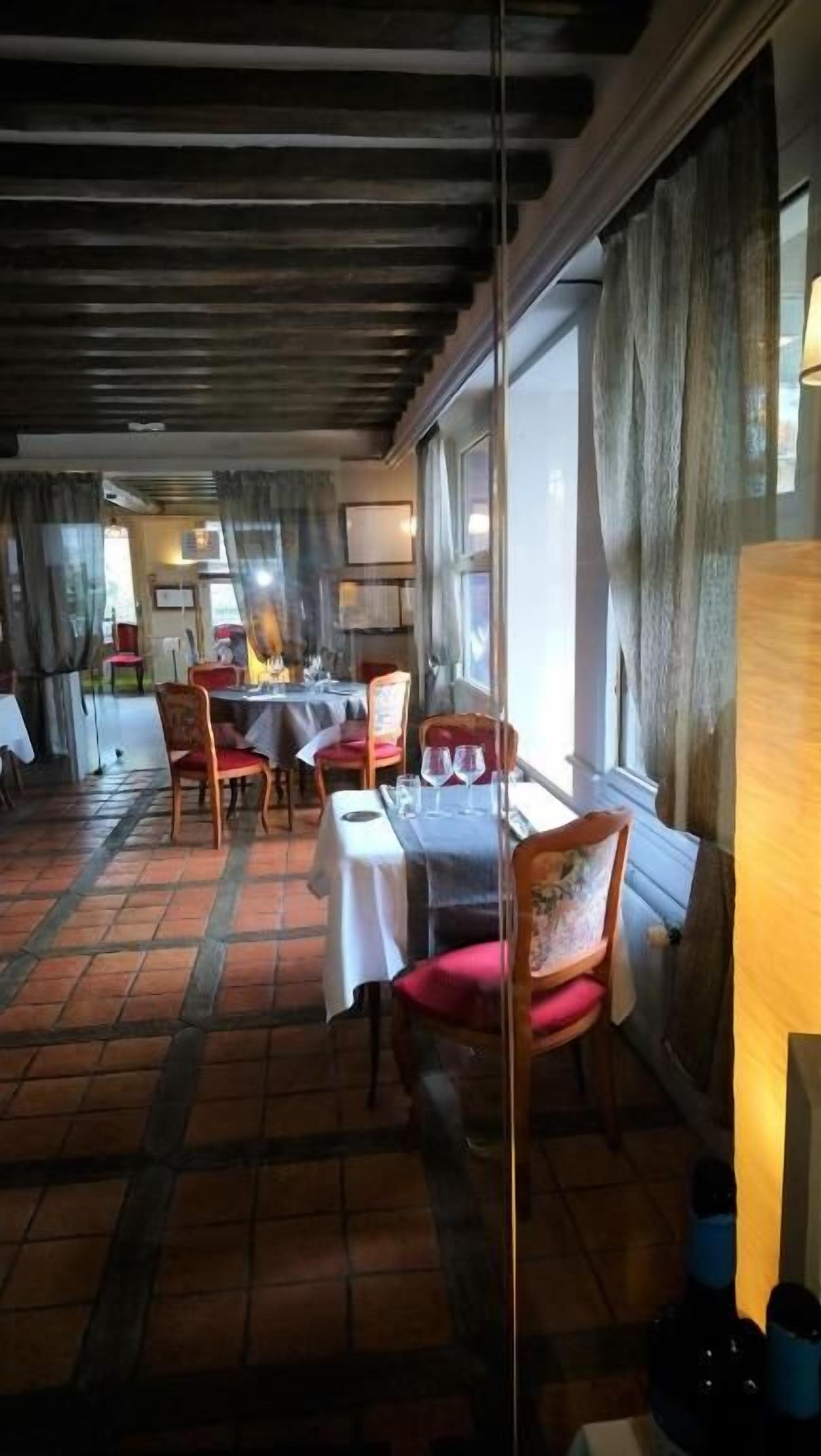 Un restaurante con vigas de madera en el techo, suelo de baldosas y mesas con sillas.