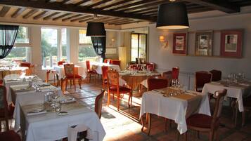 A restaurant with multiple tables set for dining, wooden chairs, and pendant lighting.