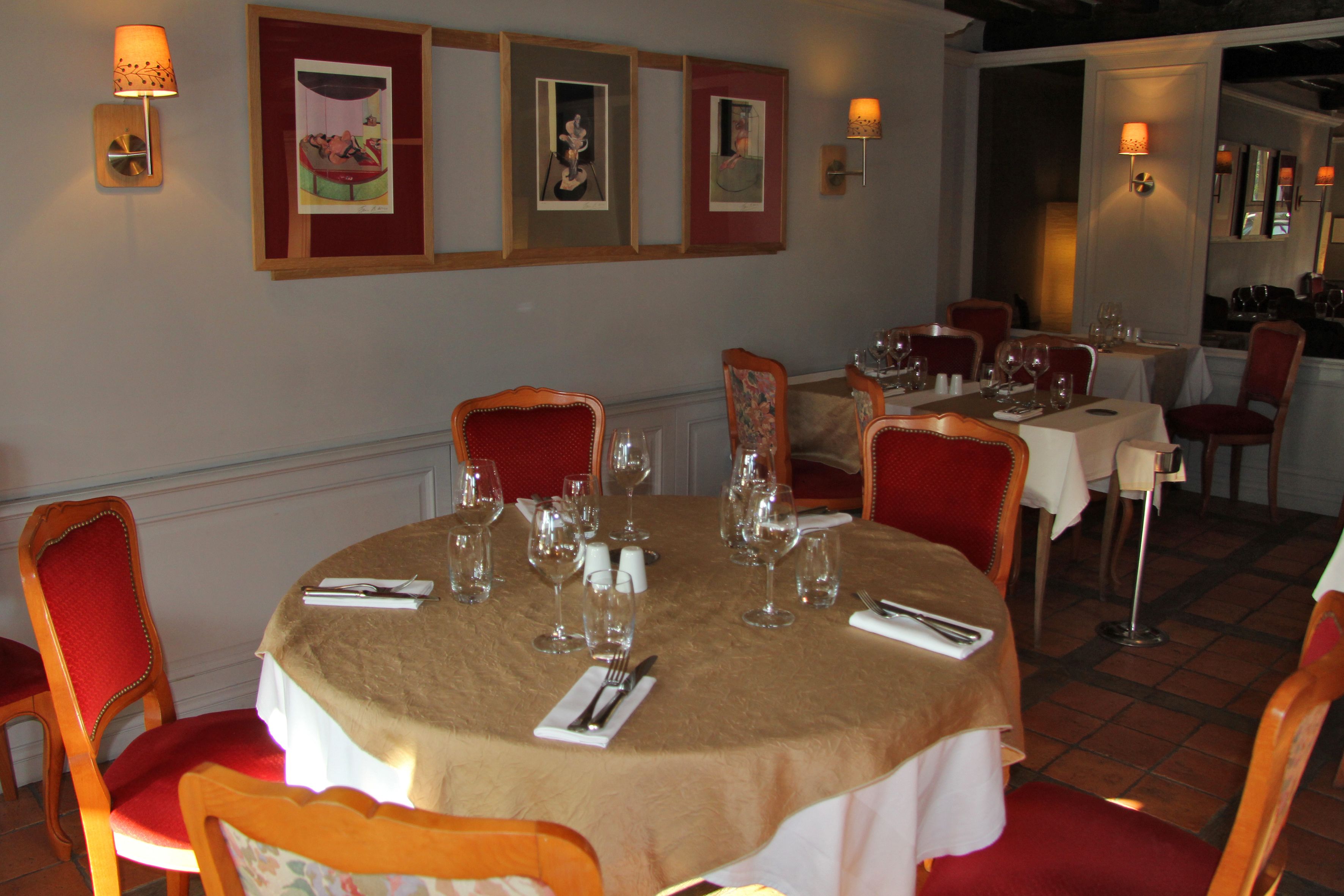 Un espace repas avec des tables rondes, des chaises à revêtement rouge et des œuvres d’art encadrées accrochées au mur.