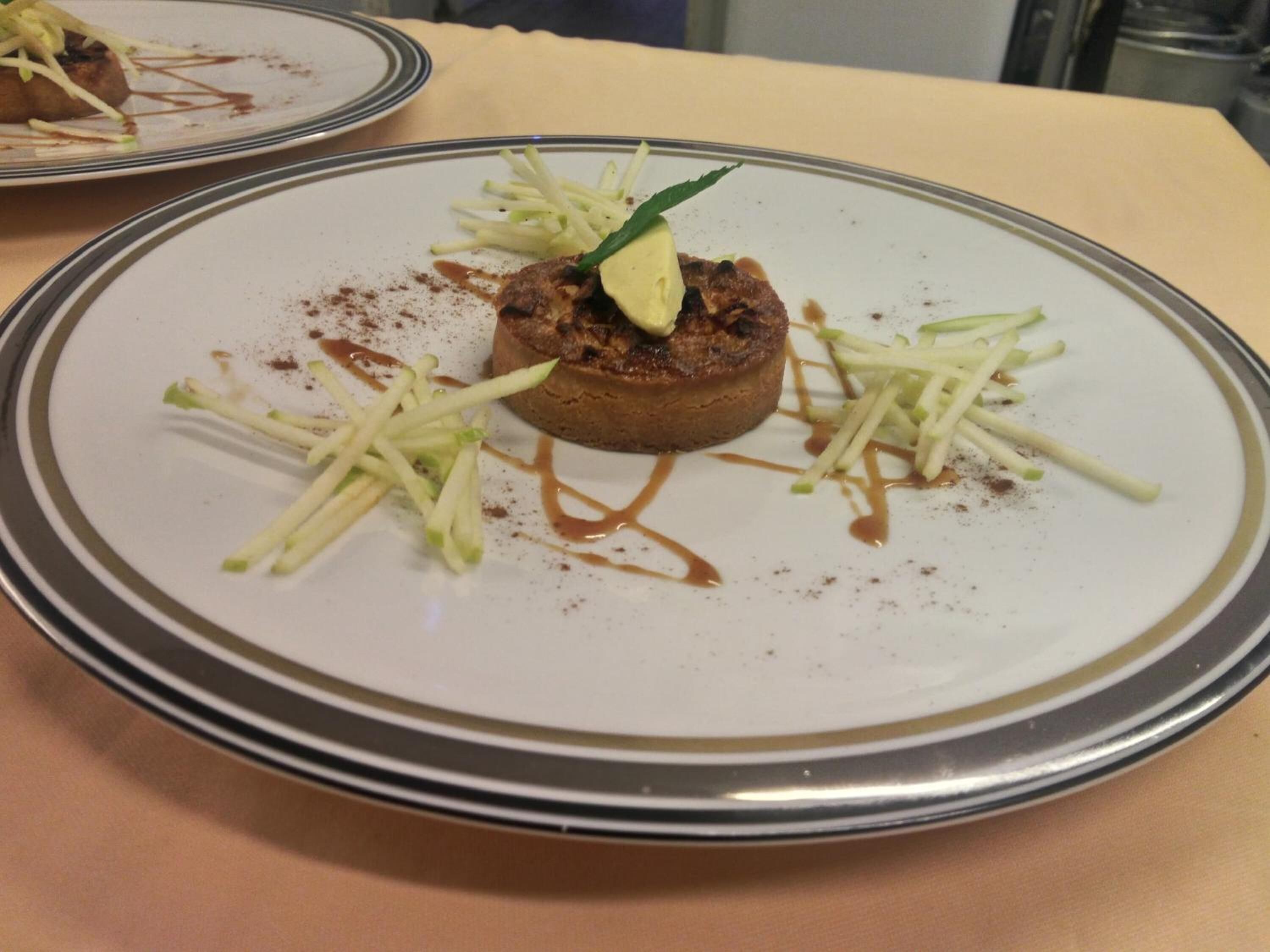 Um prato com um alimento, possivelmente um prato à carne, adornado com ervas verdes e acompanhado por legumes fatiados finamente e um molho castanho.