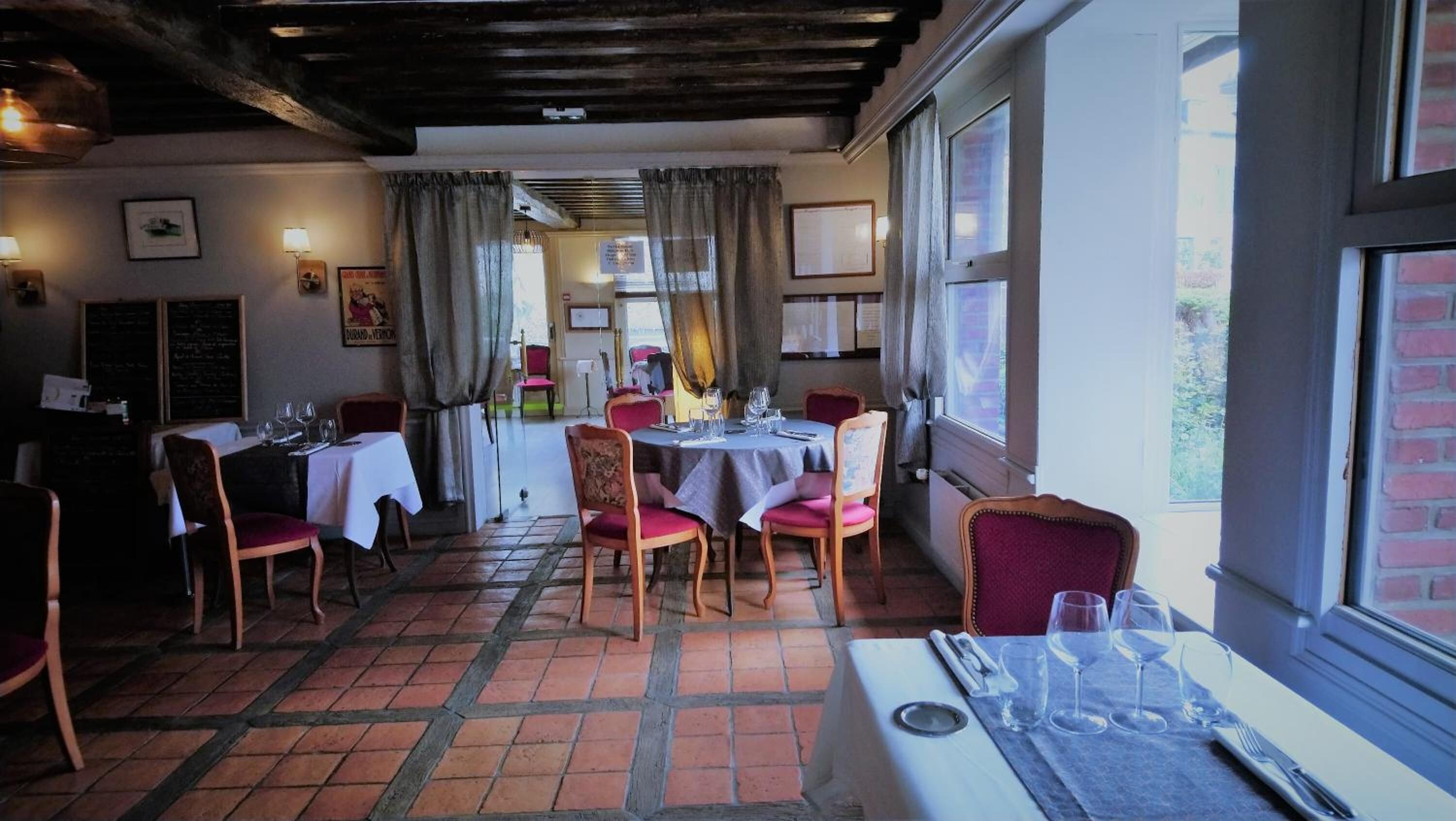 Een restaurant met een rustieke inrichting, herkenbaar aan zichtbare houten balken, betegelde vloeren en een combinatie van houten en gestoffeerde stoelen.